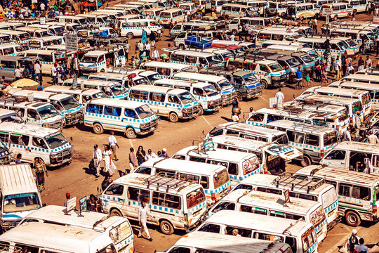 Kampala, Uganda - 28 March 2024: View of a sea of white and blue minibuses tightly packed in a bustling transportation hub, reflecting the sun's glare amidst a crowd of people..