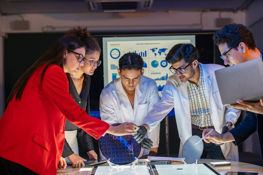 Group diverse professional scientists engineers examining silicon wafer together in laboratory research development facility semiconductor manufacturing industry technology innovation team working