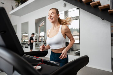 Happy woman running on a treadmill at the gym feeling healthy and fit