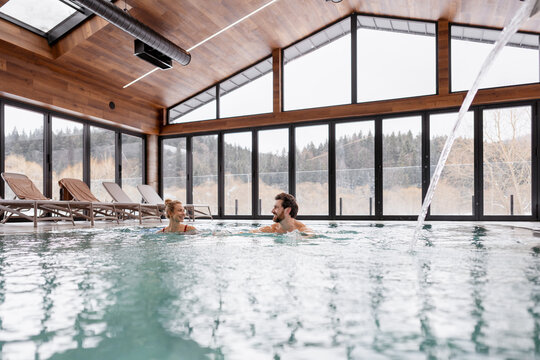 Happy couple relaxing and having fun in a modern indoor swimming pool during winter