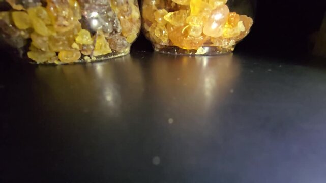 Close-up of glass jars containing high-quality Gum Arabic and Frankincense (Luban) crystals. The shot highlights the organic texture and amber-gold transparency of these natural resins.