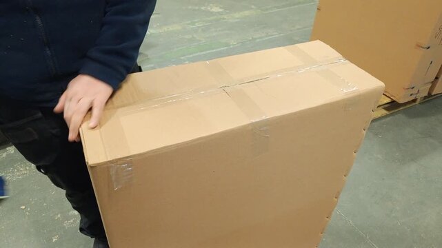 Manual packaging process of a large cardboard box with adhesive tape in a factory.