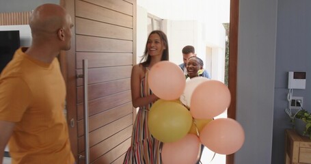 Smiling woman in striped dress greeting host in orange tee at front door, holding pastel balloons © vectorfusionart