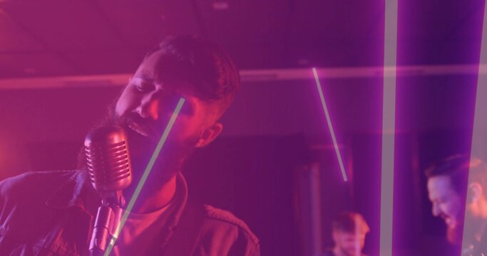 Singing singer in casual jacket leaning toward vintage mic stand on stage with LED tubes, amps
