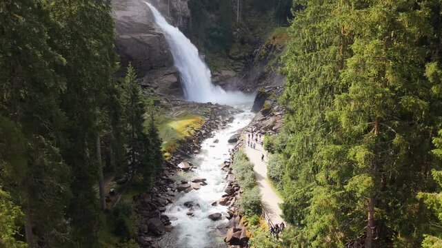 Stunning drone view of the scenic Krimmler Wasserfallweg trail. Tourists exploring the lush alpine forest and turquoise river at the base of the world-famous Austrian waterfalls in 4K