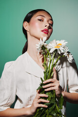 Elegant young woman with vivid red lipstick holding fresh daisies in hands, wearing soft white...