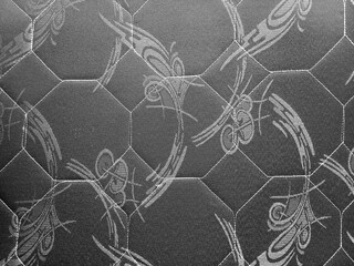 Fototapeta premium Close-up of dark grey quilted mattress fabric with hexagonal pattern and white stitching. Textile texture for bedding, furniture upholstery, and interior design.
