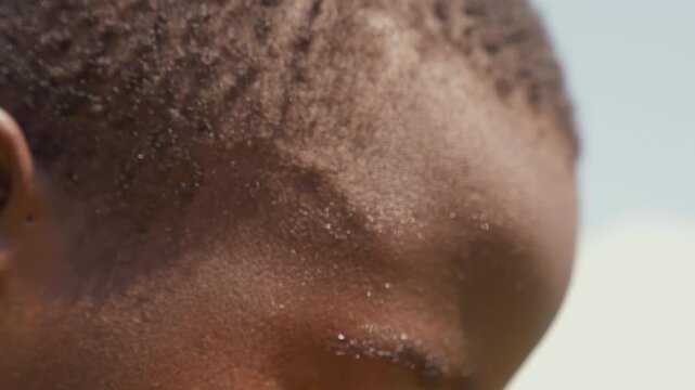 Black boy closeup with sweat, textured scalp and glistening forehead, tight crop on eye and ear, quiet postgame recovery and reflective mood, scenes imply tired trainee, recovering athlete, contender