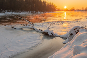 Golden sunlight bathes the icy river as it meanders through a snowy landscape