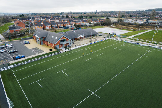 Aerial view of the expansive green sports field with rugby posts and a modern building with a car park, Blackberry Lane, Stafford, England, United Kingdom.