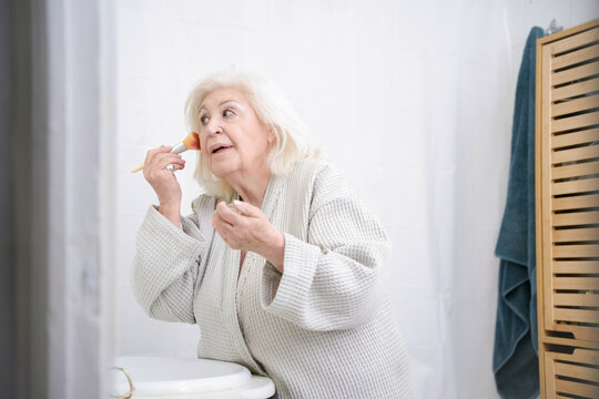 Elderly woman applying blush in bathroom