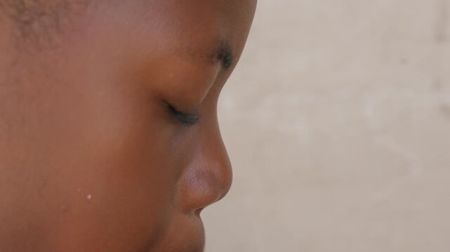 Side profile child blowing blue balloon closeup, jaw and cheek muscles visible with focused calm and breath control, silent concentration against plain textured wall, cinematic intimate study of small