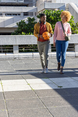 African American couple walking on plaza holding basketball, wearing headphones, carrying green bag