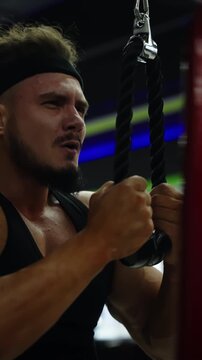 Intense cable workout sequence of a determined athlete in a dimly lit gym, shifting from strain to focused control while training upper body strength with headband and tank top