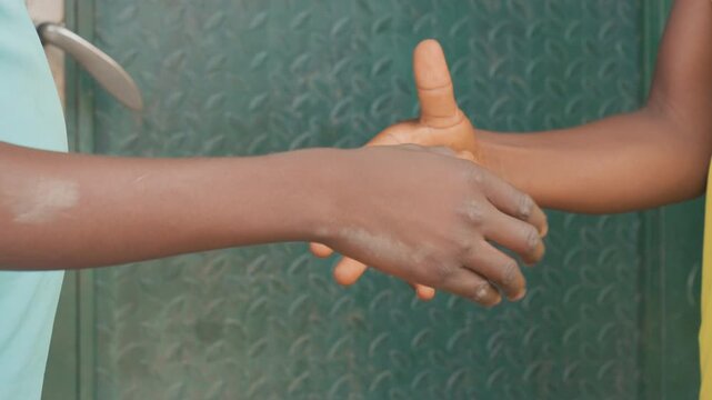 Black athletes shake hands before game closeup of two darkskinned arms locked in firm clasp against textured metal door short sleeves visible gesture of sportsmanship unity mutual respect in urban