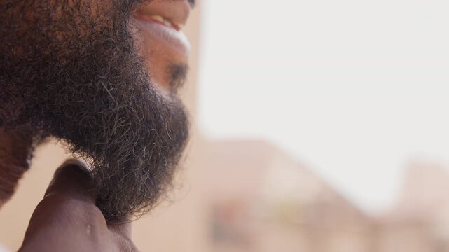 Closeup black beard hand stroking chin in soft urban light, coarse hair texture and fingers tracing jaw, intimate portrait detail showing lips and profile, quiet pregame ritual and focused