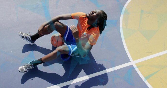 Holding knee, player wincing, sitting on outdoor blue court, orange shirt, basketball under thigh