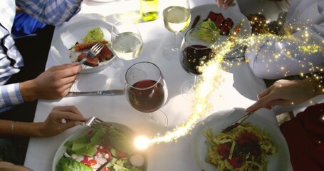 Cutting diners wearing blue shirt serving plates on white cloth, with wine and sparkling light