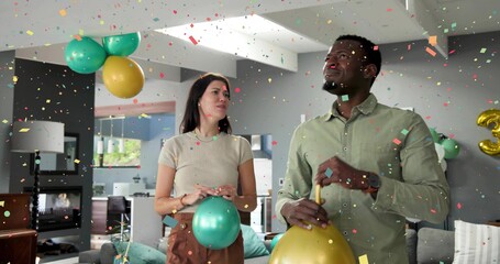 Naklejka premium Celebrating couple holding metallic balloons in living room, confetti falling, man in green shirt