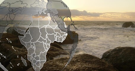 Naklejka premium Showing faint globe overlay with Africa hovering left over coast at sunset, wet rocks, choppy waves