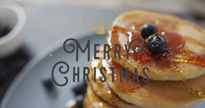 Showing pancake stack shining on tabletop with blueberries, maple syrup, Merry Christmas overlay