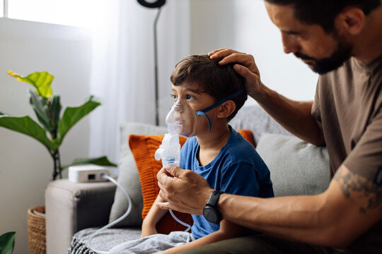 Father assisting young child during nebulizer therapy at home, showing parental care, pediatric respiratory treatment and emotional family support.