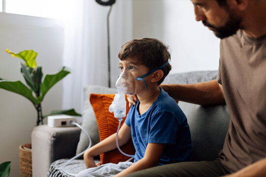 Father assisting young child during nebulizer therapy at home, showing parental care, pediatric respiratory treatment and emotional family support.