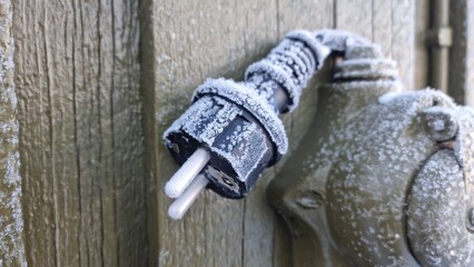 Cold weather causes frost to form on an electrical plug attached to a wall