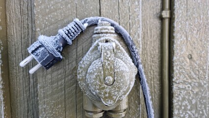Frozen electric outlet on a wooden wall during winter season