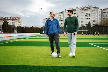 Two men walking on soccer field laughing and talking © Jelena