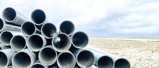 At a construction site, water pipes are neatly stacked against the backdrop of an endless sky. Modernization of the sewer and water supply system