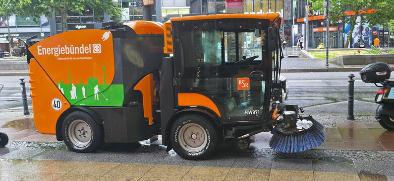 Street cleaning vehicle parked on urban street with modern buildings nearby