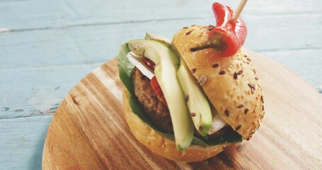 Resting seeded burger on blue table, showing avocado, greens, grilled patty, chili skewer
