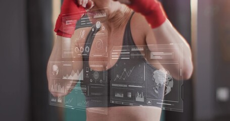 Punching mid-adult woman in sports bra delivering strike at gym, with red wraps and AR panels © vectorfusionart