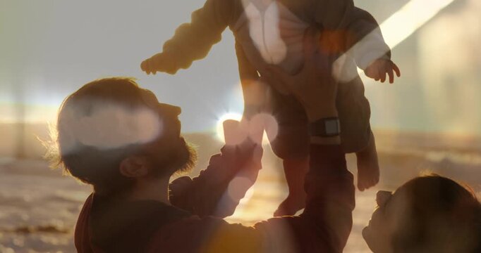 Father lifting infant on beach, raising child overhead for family bonding amid warm sun lens flare