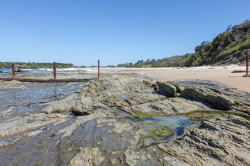 Flat rock and pools exposed by low tide at one end New Zealand beach a secluded scenic beach named after country of origin of early goldminers.