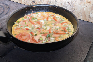 Fresh homemade omelette with tomatoes and herbs prepared in pan on old wood stove. Traditional cooking and countryside lifestyle concept.