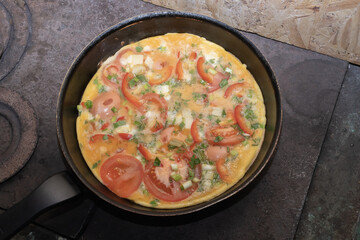 Fresh homemade omelette with tomatoes and herbs prepared in pan on old wood stove. Traditional cooking and countryside lifestyle concept.