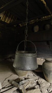 Traditional iron pot hanging on a chain above a stone hearth inside an old wooden house in ethno village Staro Selo in Sirogojno, Serbia. Authentic rural interior reflecting historic Balkan lifestyle