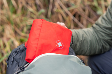 Person packing red first aid kit into backpack