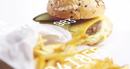 Showcasing burger on white table with sesame bun, melted cheese, pickle, blurry fries, numeric text