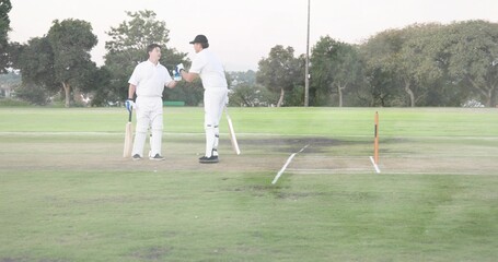 Standing two adult players nodding at cricket pitch, wearing white pads with wooden bats and stumps