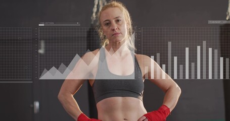 Standing boxer wearing gray sports bra and red wraps at gym with bag, showing digital charts