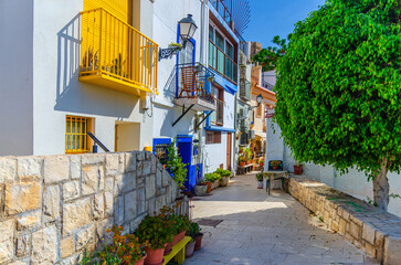 Obraz premium Alicante old town Santa Cruz with narrow street, typical white houses, traditional colorful buildings, Barri Vell Santa Creu Alacant in Alicante city historical centre, Valencian Community, Spain