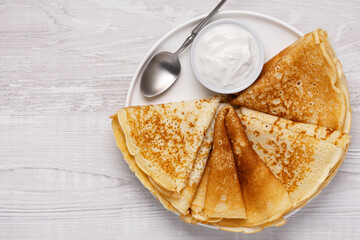 Freshly made crepes served with sour cream on a plate at a casual dining table in the morning