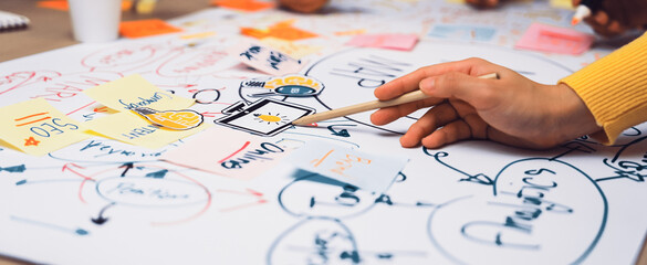 A close-up view of hands involved in brainstorming with sticky notes on chart paper, showcasing...