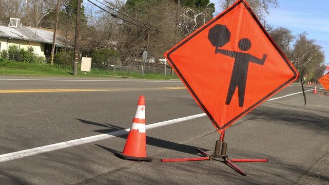 Flagman sign by side of highway with vehicle passing behind it.