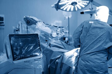A skilled surgeon in a sterile gown carefully guides a robotic arm during a knee replacement procedure. A console displays 3D models for precise surgical navigation © Damian
