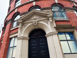 Naklejka premium Elegant red brick building in Manchester UK with ornate archway entrance and black door front