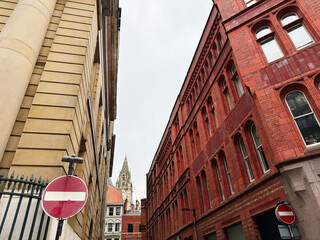 Naklejka premium Historic urban street in Manchester with red brick buildings and a distant church spire